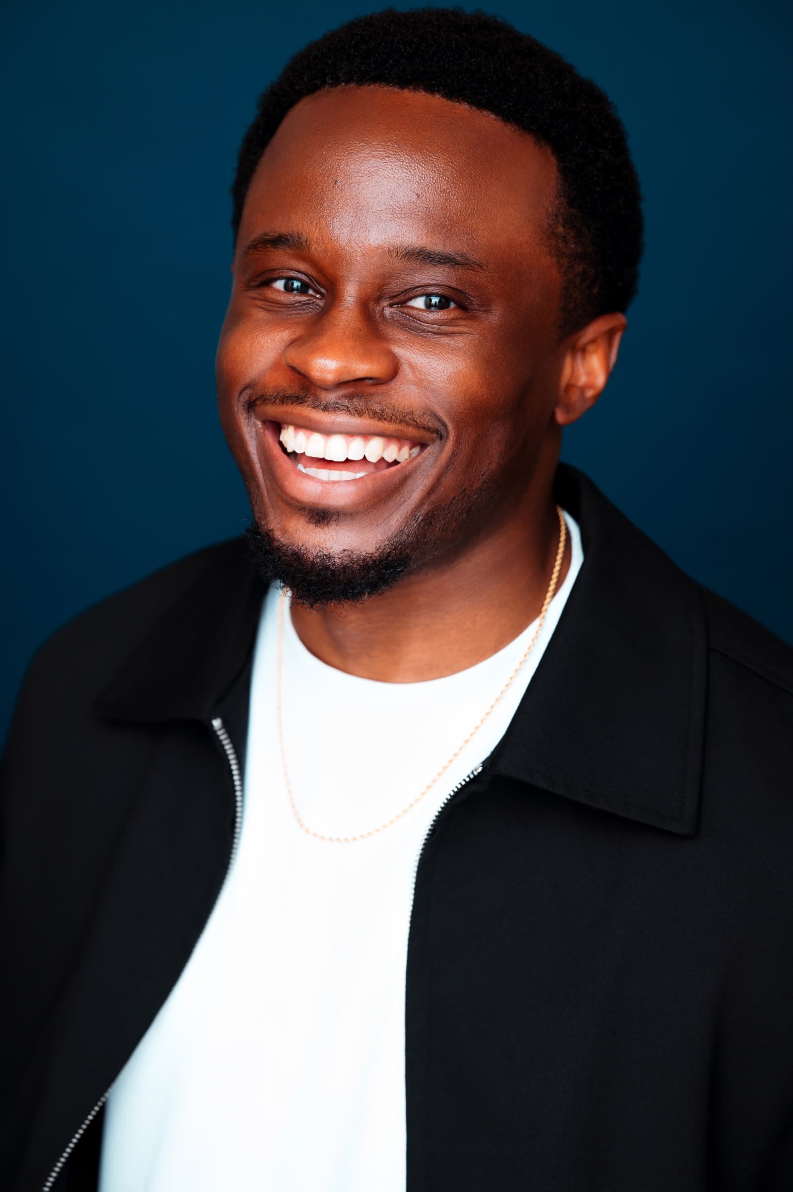 Lanre Adigun headshot — black jacket, navy backdrop
